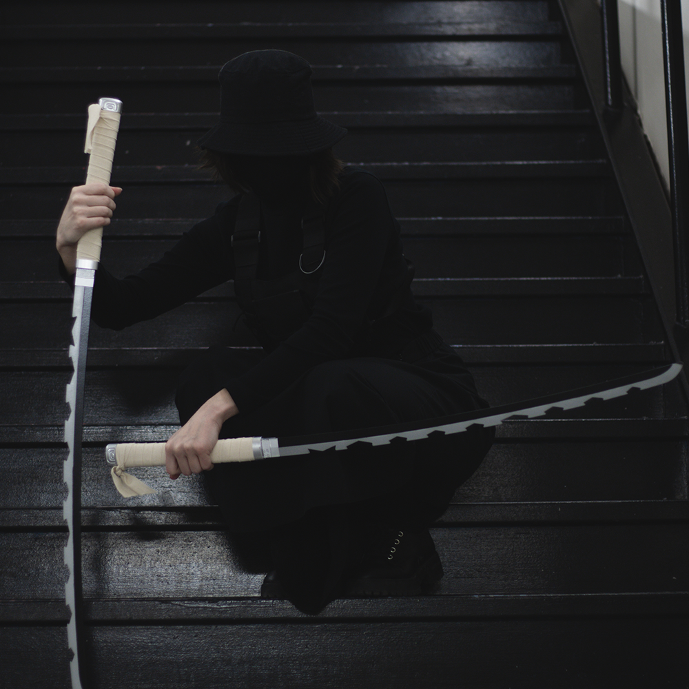 A model on a staircase weilding Inosuke Hashibara’s dual nichirin katanas - katanas with a wrapped handle and jagged blade.